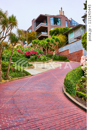 Empty curving red brick road with large brown mansion at top 115245445