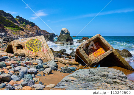 Colorful rocks around graffiti covered concrete fragments washed ashore from ocean Colorful rocks around graffiti covered concrete fragments washed ashore from ocean 115245600
