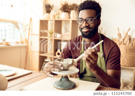 Smiling man painting pottery and looking enjoyed Smiling man painting pottery and looking enjoyed 115245700