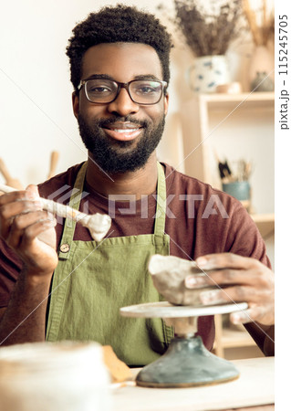 Dark-skinned bearded painting pottery and looking contented Dark-skinned bearded painting pottery and looking contented 115245705