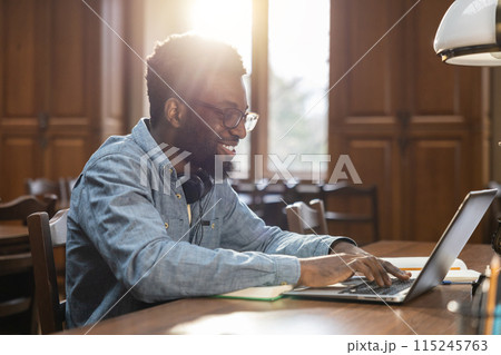 Dark-skinned young man sitting at the laptop in the library 115245763