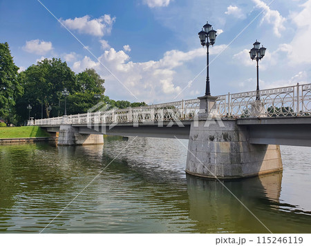 Empty pedestrian stone bridge with street lanterns on embankment of Upper Lake - artificial city pond, popular recreation zone in Kaliningrad, Russia at sunny summer day. With no people cityscape. 115246119