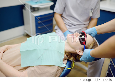 Practitioner dentist doctor prepares woman for teeth treatment in hospital. Assistant wearing protection glasses on patient before orthodontists or prosthetics treatment in modern medical center Practitioner dentist doctor prepares woman for teeth treatment in hospital. Assistant wearing protection glasses on patient before orthodontists or prosthetics treatment in modern medical center 115247210