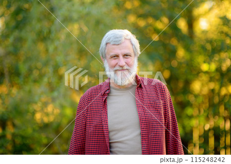 Portrait of mature handsome gardener on sunny summer day. Grey hair senior man farmer is on his own garden. 115248242