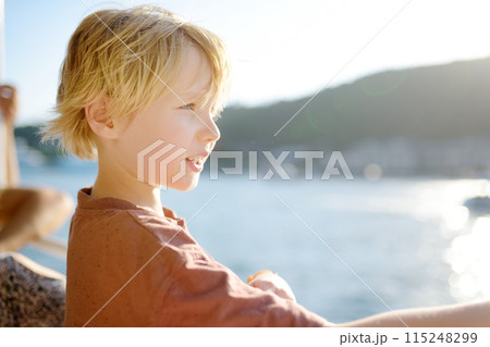 Cute blonde preteen boy is traveling by boat or ferry on the sea. Family vacations on ocean or sea. Summer leisure for families with kids. 115248299
