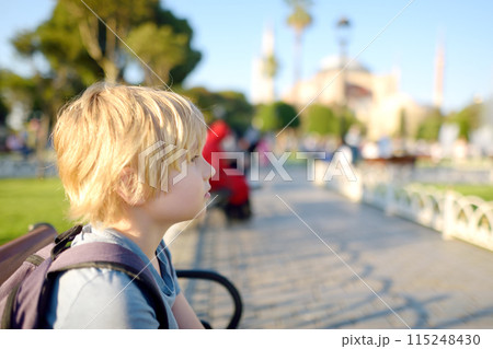 Cute blonde preteen tourist boy sitting on a bench near Sultan Ahmed Mosque district on background of Hagia Sophia Mosque on sunny summer day. Travel, tourism, sightseeing in Istanbul, Turkey. Cute blonde preteen tourist boy sitting on a bench near Sultan Ahmed Mosque district on background of Hagia Sophia Mosque on sunny summer day. Travel, tourism, sightseeing in Istanbul, Turkey. 115248430