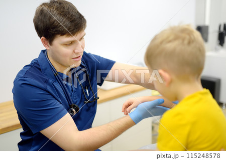 A cute toddler boy with his mother are at an appointment with a pediatrician. The doctor orthopedist is examines joints of a little patient. A cute toddler boy with his mother are at an appointment with a pediatrician. The doctor orthopedist is examines joints of a little patient. 115248578