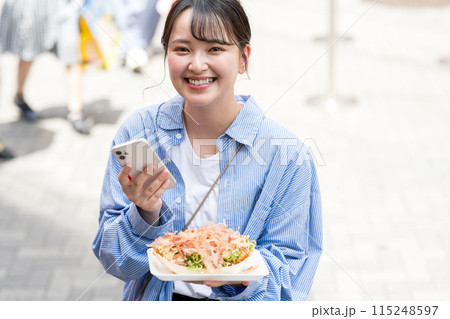 明るい屋外でたこ焼きをスマホで撮影する若くて可愛いSNS好きな女性|大阪府大阪市道頓堀商店街 明るい屋外でたこ焼きをスマホで撮影する若くて可愛いSNS好きな女性|大阪府大阪市道頓堀商店街 115248597