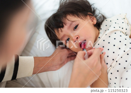 mother feeding liquid medicine to baby girl by syringe. sick crying toddler mother feeding liquid medicine to baby girl by syringe. sick crying toddler 115250323