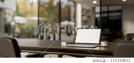A laptop computer white-screen mockup on a meeting table in a modern meeting room. 115250612