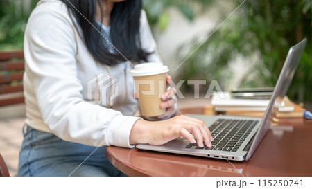 A woman is typing on her laptop computer, sipping coffee, working remotely at a cafe. 115250741