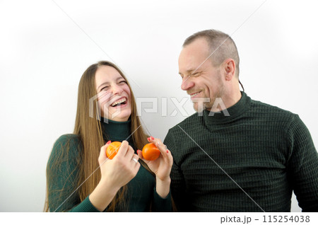 Happy laughing couple kissing in slowmo talking and peeling tangerines. Pregnant Caucasian wife and smiling husband enjoying Christmas celebration at home indoors. 115254038