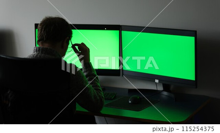 close-up green screens of two monitors man in dark sits with back ad optics space for text online training computer programs fatigue rest time to travel soon weekend working days office weekdays 115254375