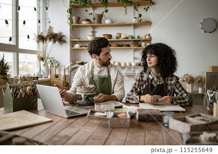 Mature man and young woman sculpting clay in pottery workshop 115255649
