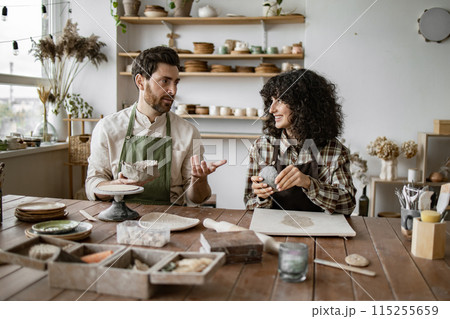Mature man and woman sculpting clay pottery in studio 115255659