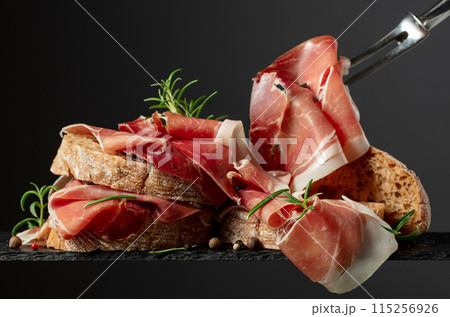 Ciabatta with prosciutto and rosemary on a black background. 115256926