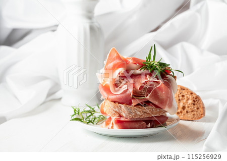 Ciabatta with prosciutto and rosemary on a white wooden table. 115256929