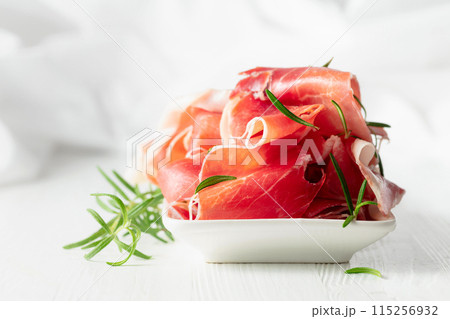 Prosciutto with rosemary on a white wooden table. Prosciutto with rosemary on a white wooden table. 115256932