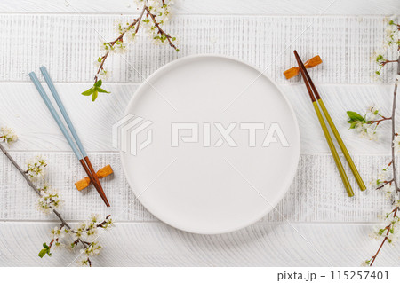 Table adorned with cherry blossom branch and chopsticks, epitomizing Japanese food culture Table adorned with cherry blossom branch and chopsticks, epitomizing Japanese food culture 115257401