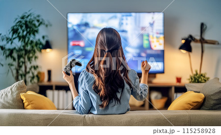 家庭用ゲームのコントローラーを使って夜にリビングで遊ぶ女性 115258928