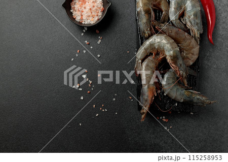 Large king prawns raw on a black cutting board. Hot pepper, salt. Black background 115258953