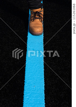 Asphalt road with blue lane and a person with boots walking on it. Asphalt road with blue lane and a person with boots walking on it. 115261068