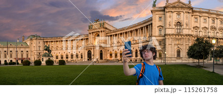Vienna, Austria, August 17, 2022. Magnificent view of the Hofburg Imperial Palace at sunset, the warm evening light enhances the impressive facade. A young man takes a selfie. Large format shot. Vienna, Austria, August 17, 2022. Magnificent view of the Hofburg Imperial Palace at sunset, the warm evening light enhances the impressive facade. A young man takes a selfie. Large format shot. 115261758