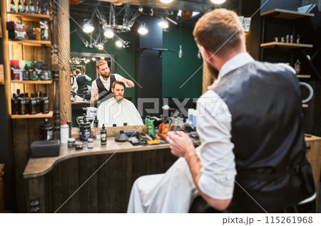 Hairdresser making final touches in new haircut. Comfortable atmosphere in modern barbershop. Hairdresser making final touches in new haircut. Comfortable atmosphere in modern barbershop. 115261968