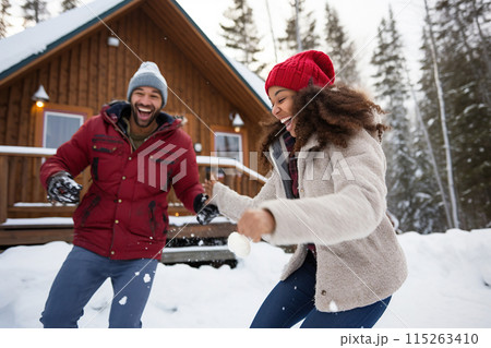 Joyful couple having energy snowball fight outside winter holiday log cabin 115263410