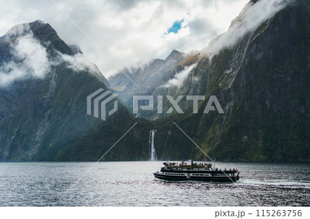 Ferry cruising with mountain and waterfall flowing in fjord at Milford Sound, New Zealand 115263756