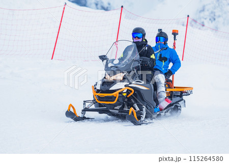 Rescuer man driving snowmobile with patient on the ski resort. 115264580