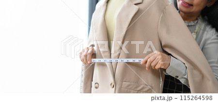 Skilled senior tailor working in the workshop studio measuring a jacket on a mannequin with tape measure 115264598