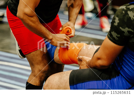 coach applies an knee elastic wraps to athlete before barbell squat coach applies an knee elastic wraps to athlete before barbell squat 115265631