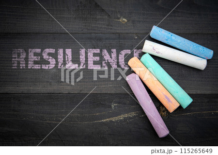 Resilience concept. Text and pieces of chalk on a dark wood texture background Resilience concept. Text and pieces of chalk on a dark wood texture background 115265649
