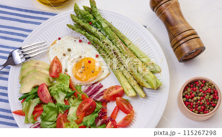Round plate with cooked asparagus, fried egg, avocado and fresh vegetable salad on the table 115267298