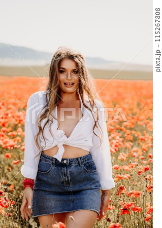 Happy woman in a poppy field in a white shirt and denim skirt with a wreath of poppies on her head posing and enjoying the poppy field. 115267808