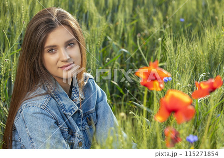 Brunette girl dressed in jeans sitting in cornfield with red poppies. 115271854