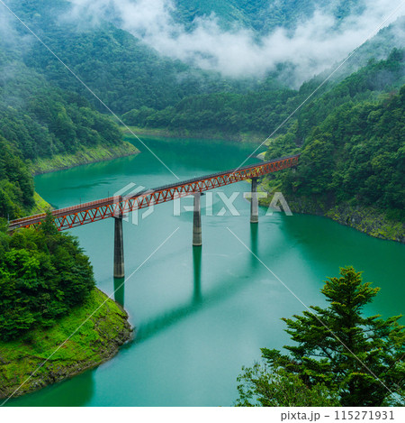 beautiful red railroad bridge crossing over mountain lake 115271931