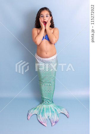 Beautiful surprised girl in mermaid costume stand on blue background 115272022