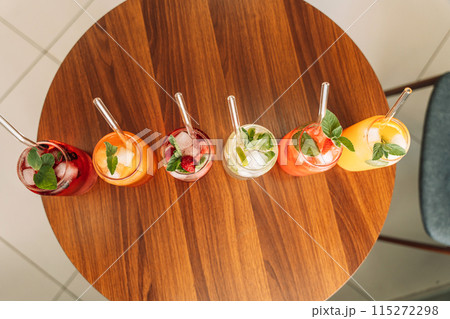 Fruit drinks with berries and ice in glass glasses and straws on a wooden table 115272298