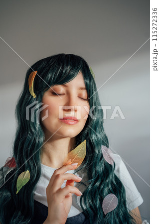 Beautiful tender woman with long dark green hair and multicolored skeleton leaves in ray of sunset light. Attractive fantasy girl, Young elven princess style. A gentle image. Autumn, fall concept. 115272336