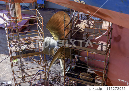 Cargo vessel in dry dock on ship repairing yard. Variable pitch propeller and rudder. Welder working on ship repairing yard. Cargo vessel in dry dock on ship repairing yard. Variable pitch propeller and rudder. Welder working on ship repairing yard. 115272983