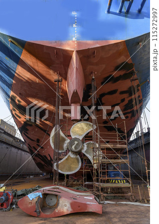 Cargo vessel in dry dock on ship repairing yard. Variable pitch propeller and rudder. Welder working on ship repairing yard. Cargo vessel in dry dock on ship repairing yard. Variable pitch propeller and rudder. Welder working on ship repairing yard. 115272997
