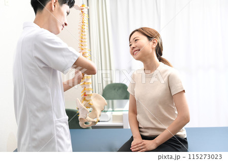 骨の模型を使い女性患者に説明する男性医師 115273023