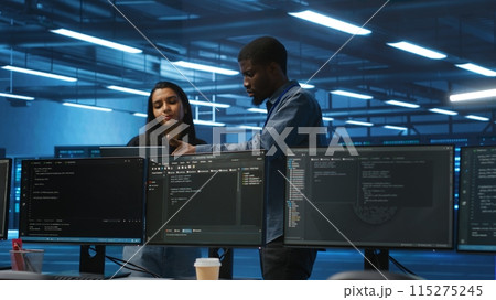Multiethnic team of engineers uses laptop to do programming for servers providing computing resources for different workloads. Diverse colleagues using notebook to supervise data center supercomputers 115275245