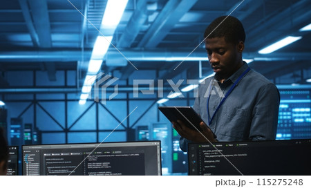 Technician in server hub using tablet to find hardware misconfigurations affecting rackmounts performance. Man checking data center infrastructure devices bottlenecks leading to errors Technician in server hub using tablet to find hardware misconfigurations affecting rackmounts performance. Man checking data center infrastructure devices bottlenecks leading to errors 115275248