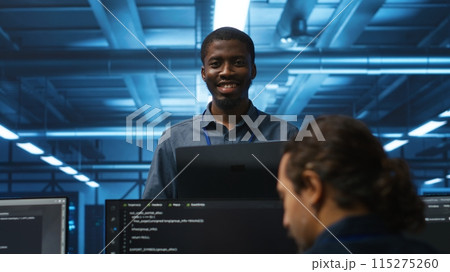 Portrait of cheerful african american manager supervising team in server room providing computing resources for workloads. Jolly supervisor oversees technicians in data center mending supercomputers 115275260