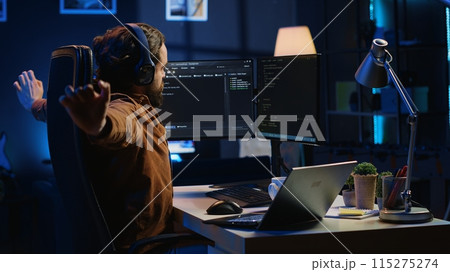 Software programmer taking break from coding, putting headphones on and stretching on desk chair during remote job shift. IT professional pausing tasks, listening music, loosening up, camera A Software programmer taking break from coding, putting headphones on and stretching on desk chair during remote job shift. IT professional pausing tasks, listening music, loosening up, camera A 115275274