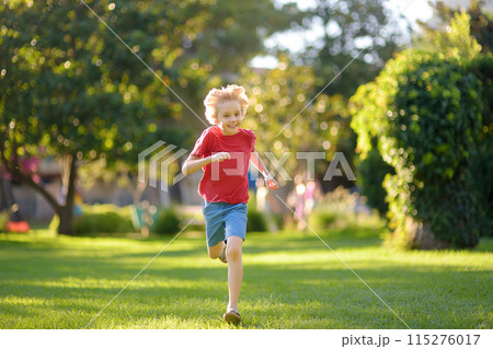 Elementary school child running on lawn in urban park on sunny day. Happy preteen boy having fun during walk. Outdoors activity for kids on summer holidays 115276017