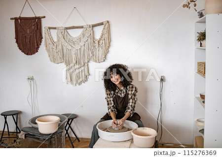 Female potter crafting ceramic bowl on wheel in cozy studio Female potter crafting ceramic bowl on wheel in cozy studio 115276369